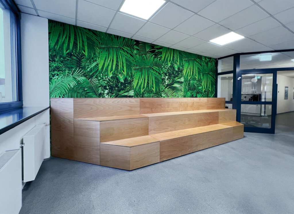 Stufenförmiges Holzpodest vor grüner Pflanzenwand in einem modernen Büro